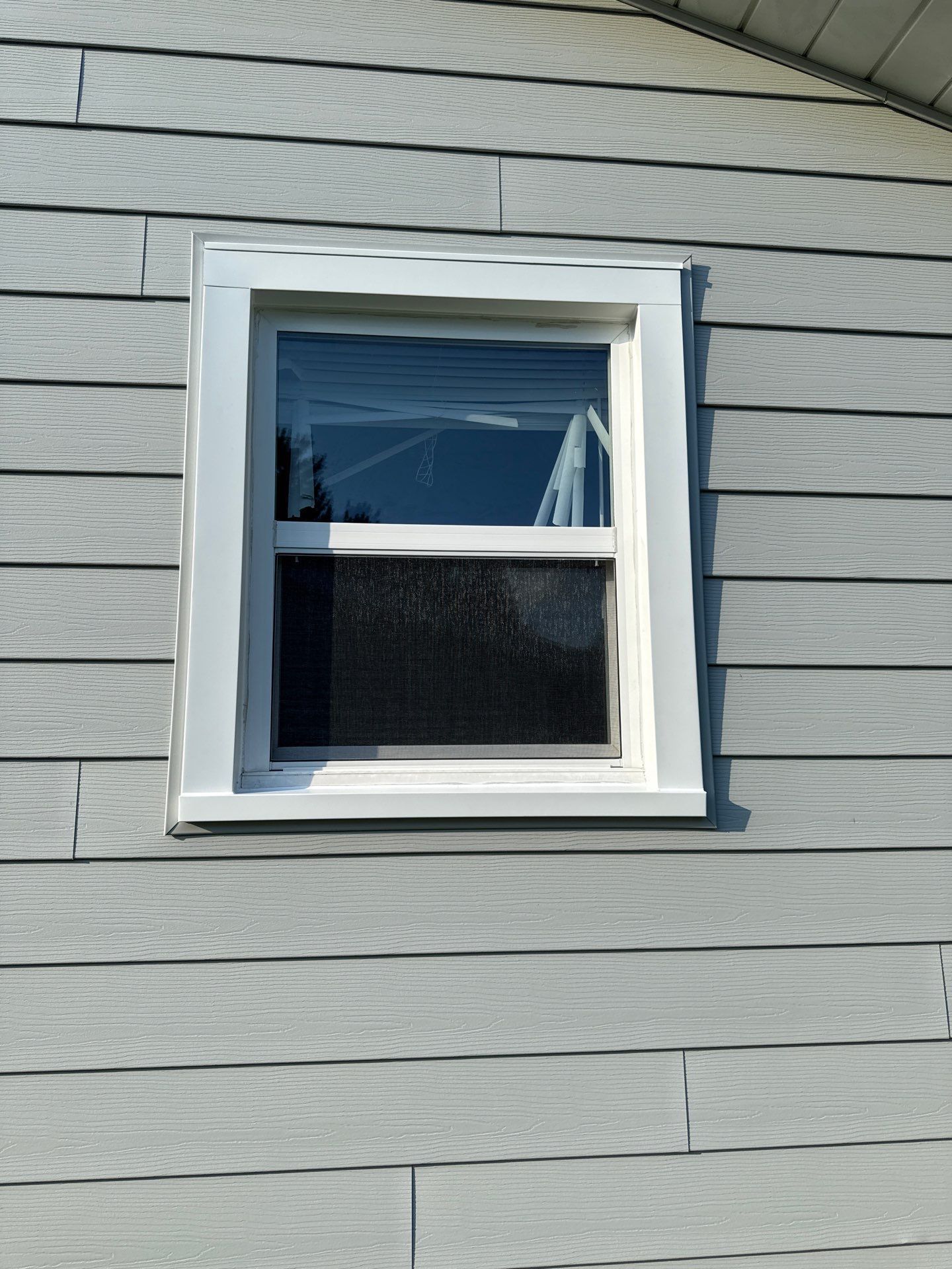 White-framed window on a gray-sided house. The window reflects sky and interior darkness.