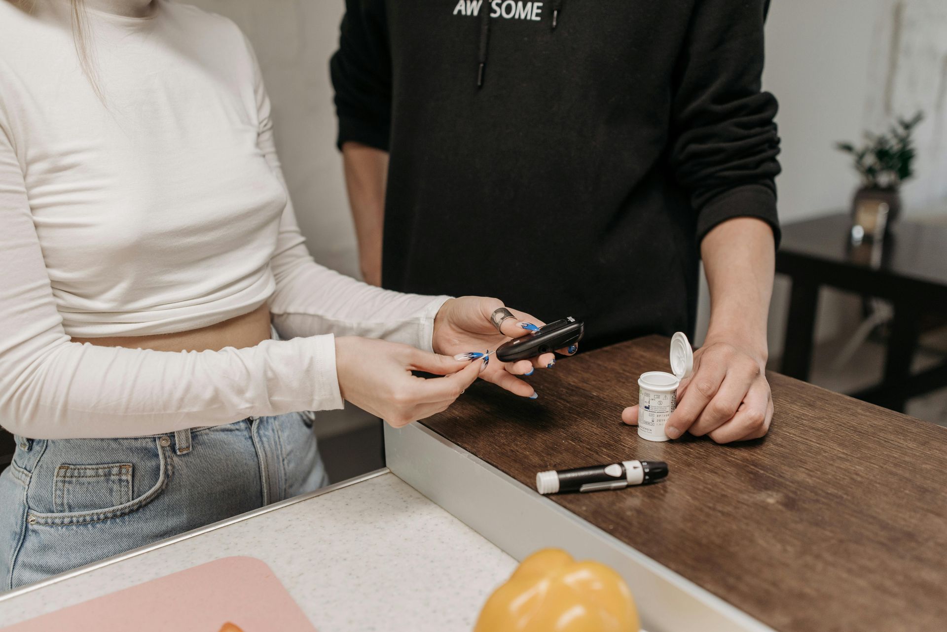 Two people at a kitchen counter comparing a smartphone near small bottles and a vape device