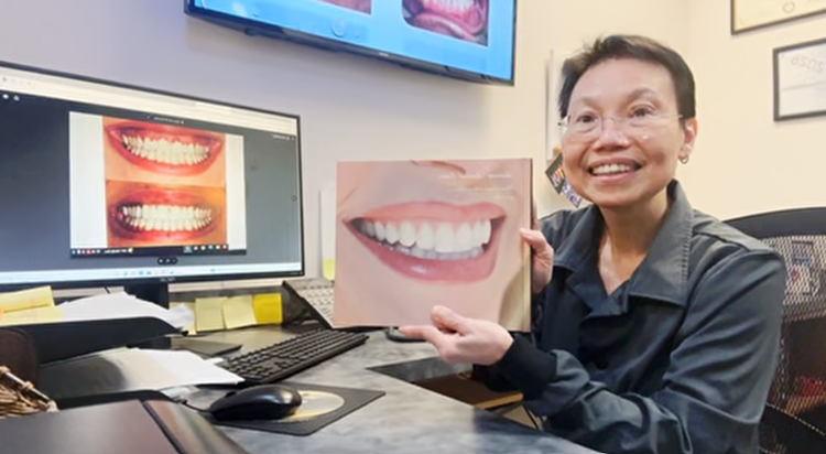 Person at a desk holding a photo of a smile with dental images on a computer screen