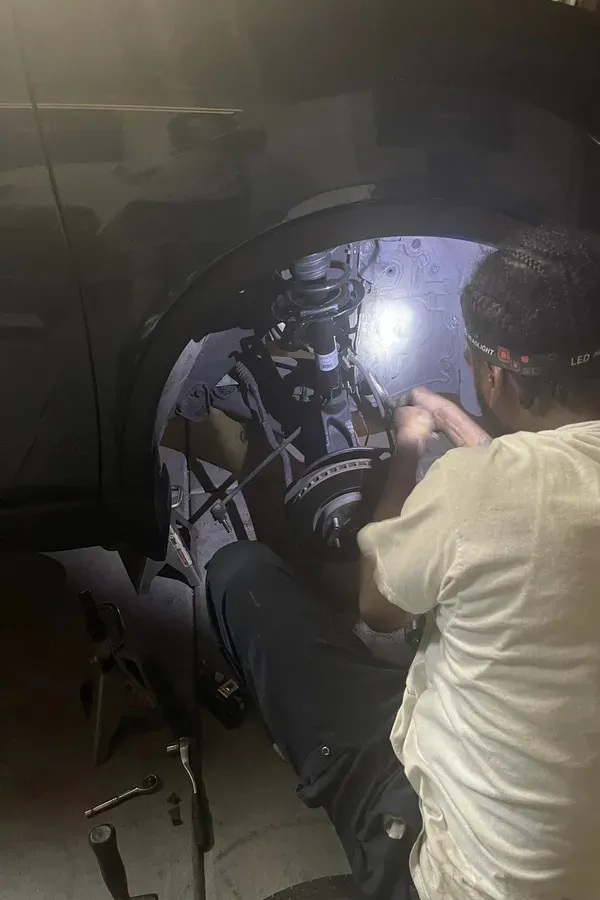 Person washing the front wheel of a black car in a dim garage, with water and soap suds visible.