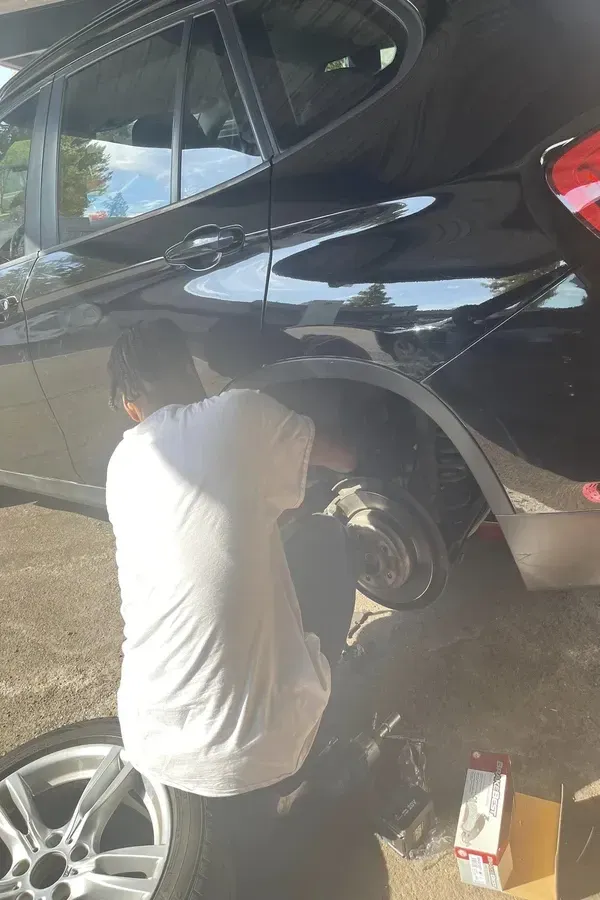 Person changing a car tire on a black SUV in a driveway, with tools and a spare wheel nearby