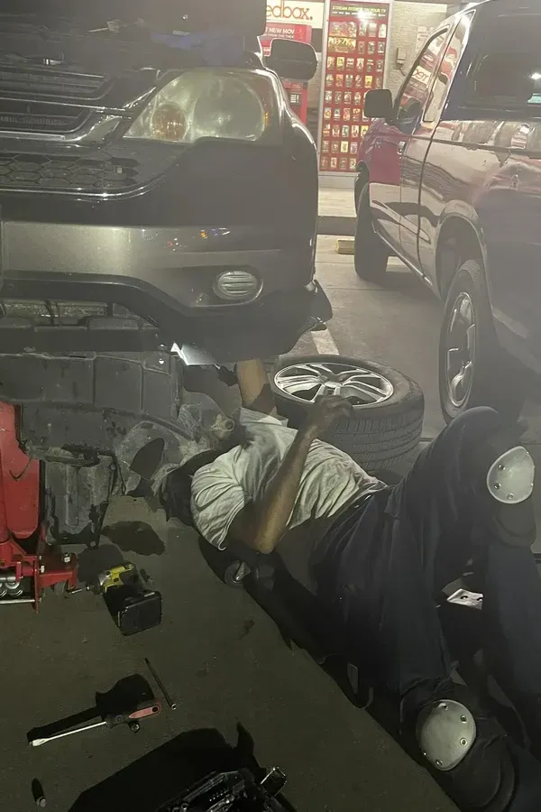 Mechanic lying under a car in a garage, working with tools and parts on the floor.