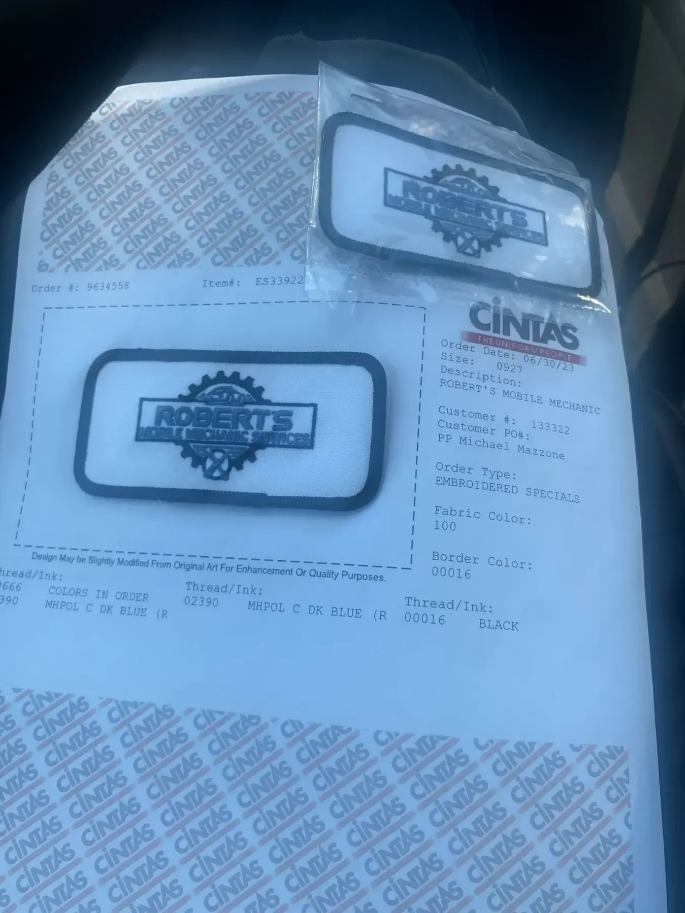 Two Cintas uniform patches on a printed receipt, lying on a car seat.