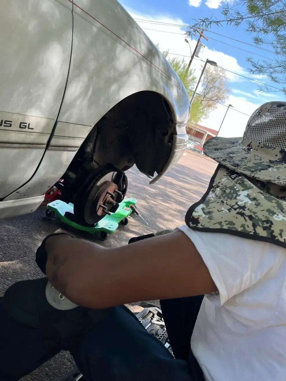 Two people leaning over a dog on a green mat beside a vehicle outdoors