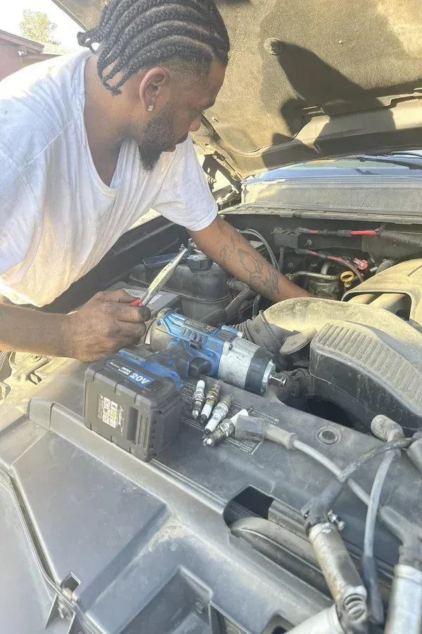 Person working on a car engine under the open hood, using blue gloves in a garage.