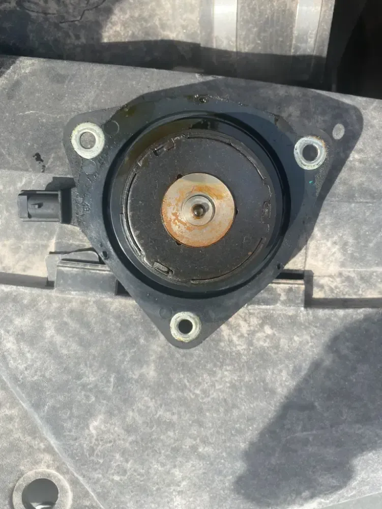 Close-up of a black circular speaker mount with three screw holes and a copper center on a gray surface