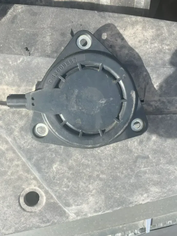 Black round plastic mechanical part with three bolt holes on a gray surface