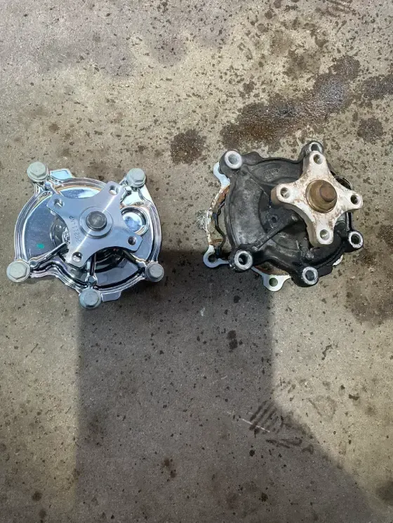 Two metal mechanical parts on a concrete floor, one shiny silver and one dark, with a shadow between them