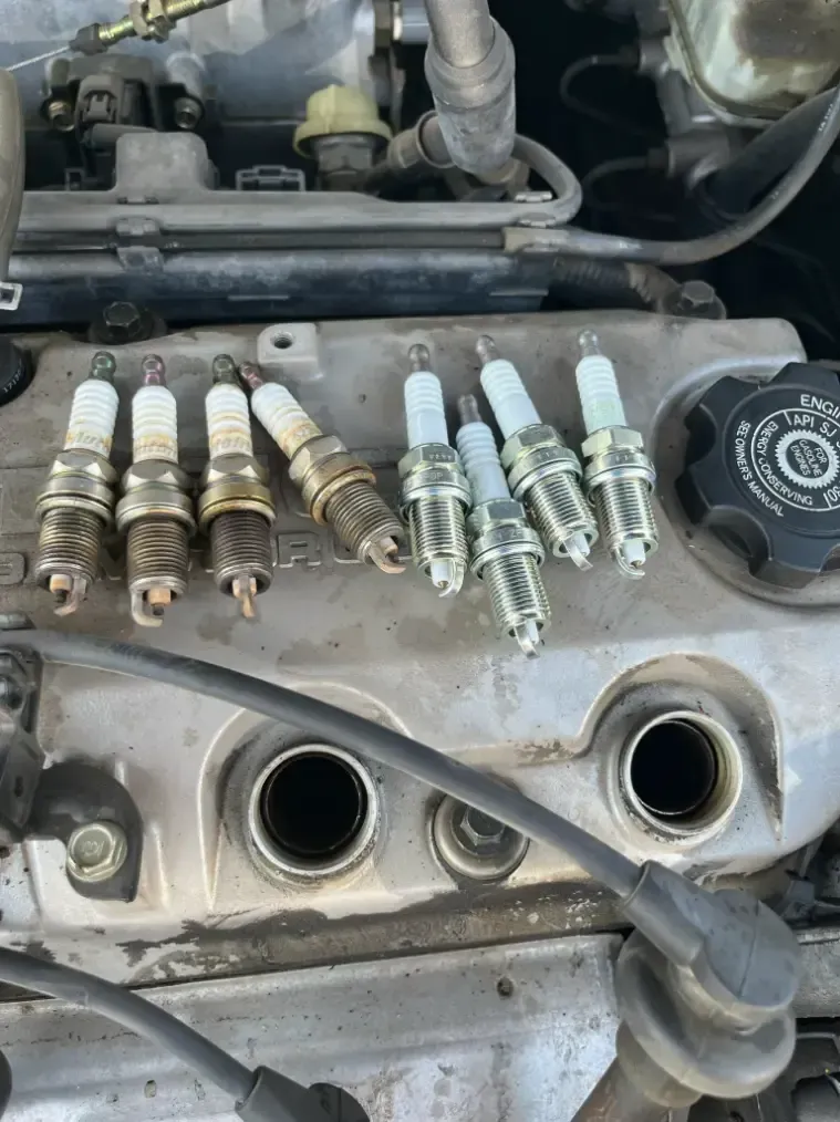Spark plugs laid across an exposed car engine cylinder head with visible spark plug ports.
