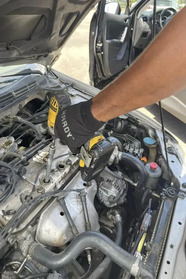 Mechanic’s gloved hand working in a car engine bay with the hood open.