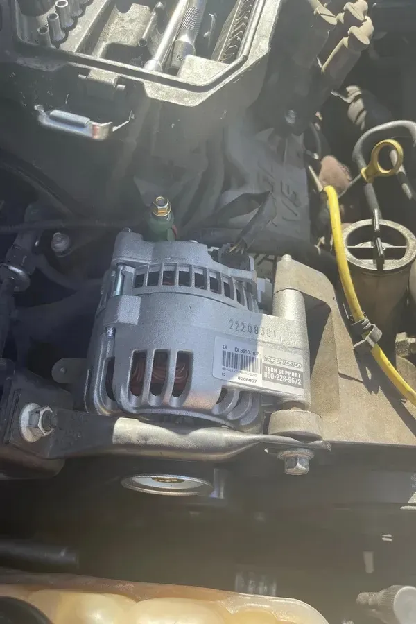 Close-up of a car engine bay with a gray alternator and yellow dipstick handle