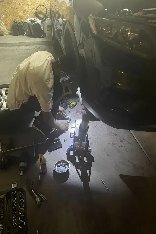 Person working under a car in a garage with tools and a bright work light