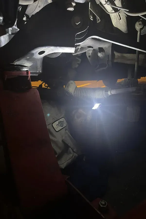 Dark engine bay with a bright flashlight illuminating car parts and wires