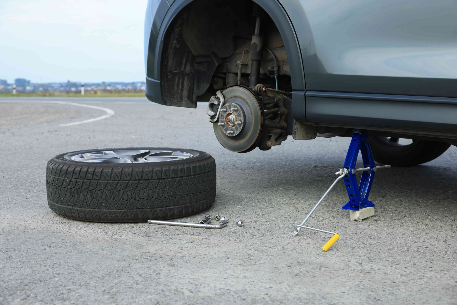 Car with front wheel removed on a jack beside a detached tire on pavement.
