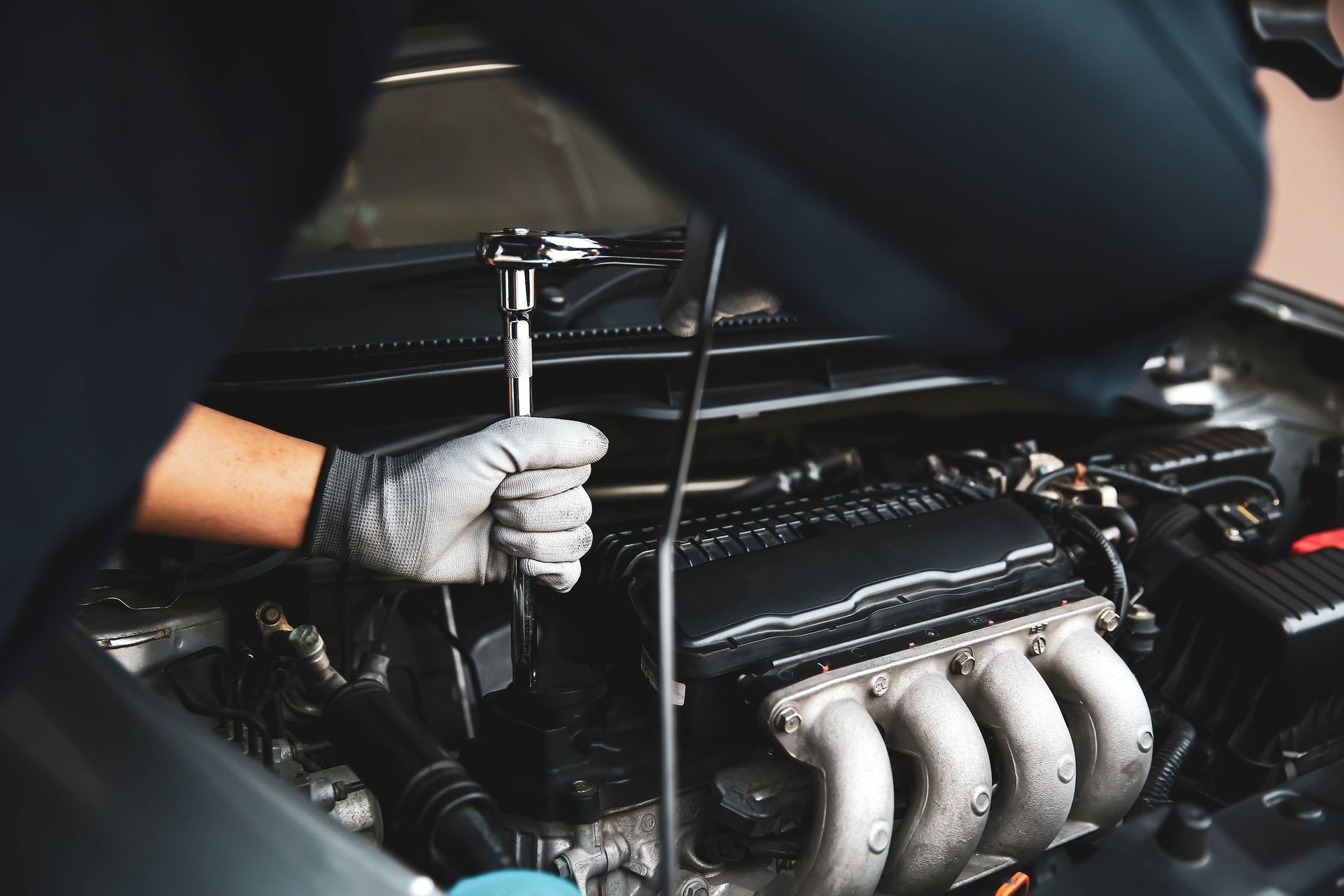 Gloved hands tightening a bolt on a car engine in a garage