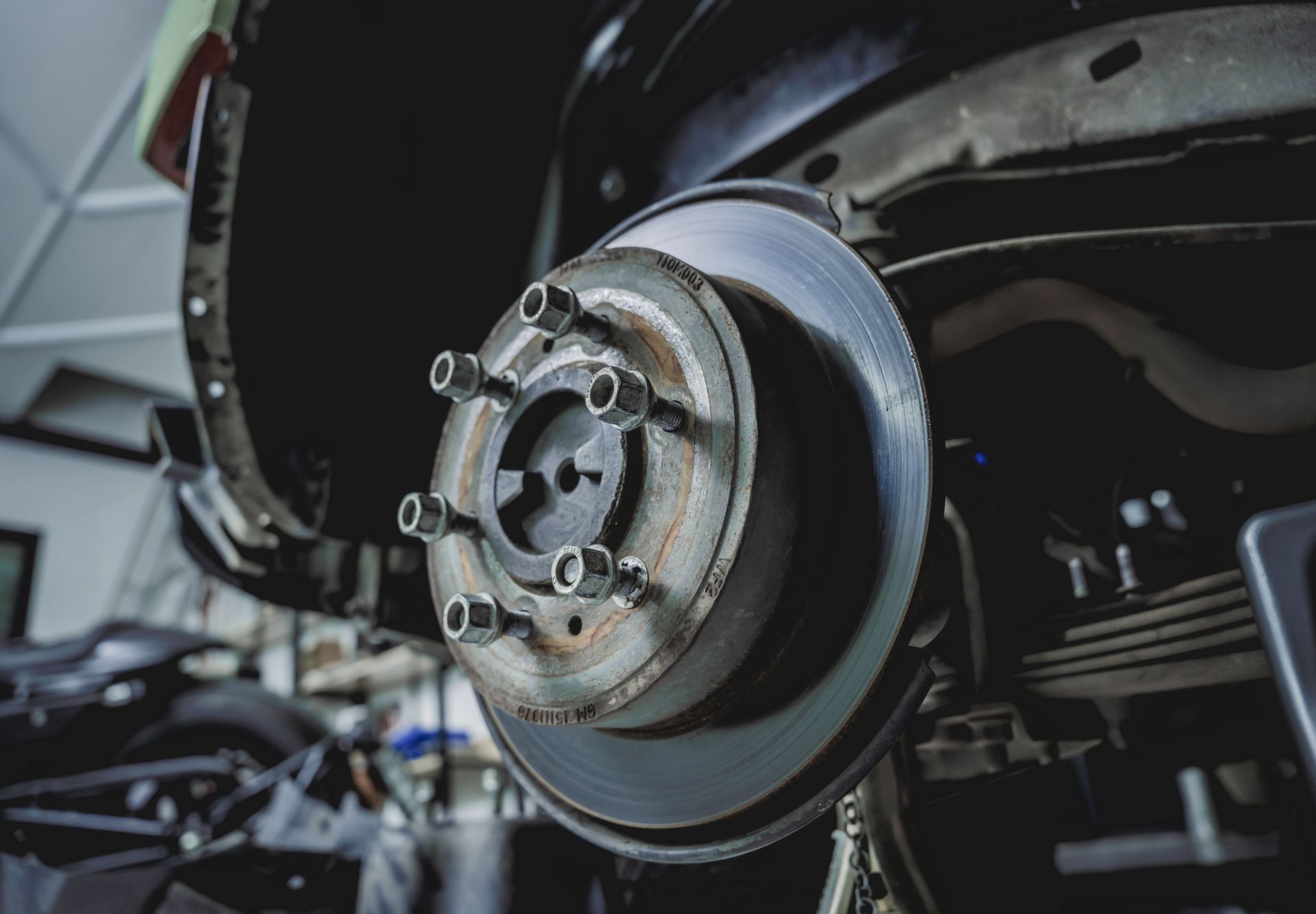 Close-up of a car’s exposed brake disc and wheel hub during repair in a garage