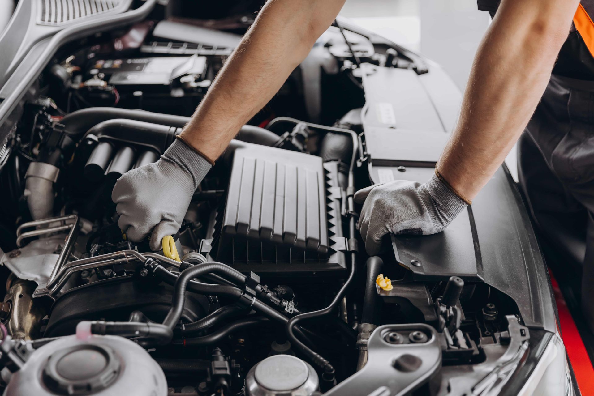 Mechanic’s gloved hands working under a car hood in an engine bay