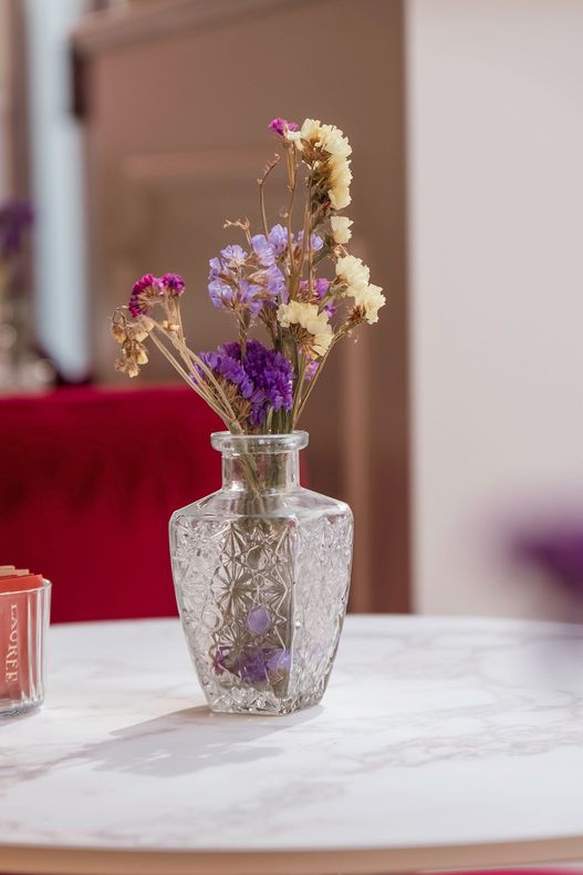Vaso di vetro con fiori secchi viola e color crema su un tavolo bianco
