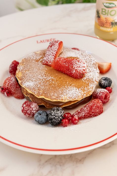 Due persone sedute a un tavolo di marmo mangiano pile di pancake guarniti con sciroppo al cioccolato, fragole e mirtilli.