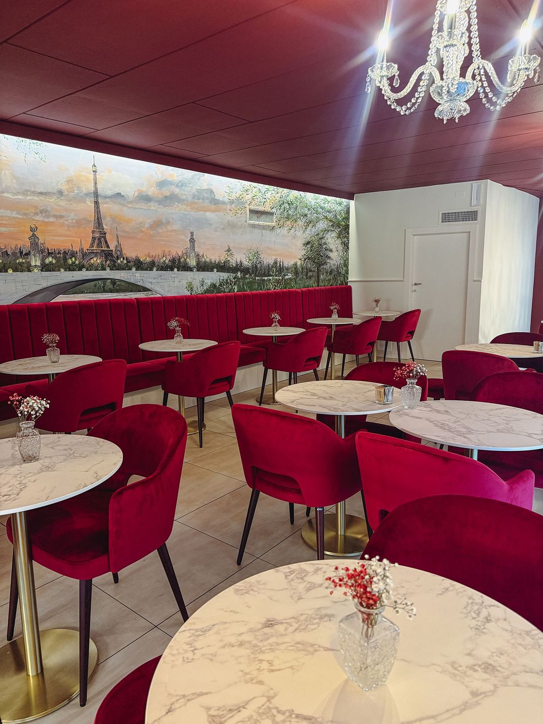 L'interno di un caffè è caratterizzato da sedie in velluto rosso, tavoli con piano in marmo e un grande murale della Torre Eiffel sulla parete.