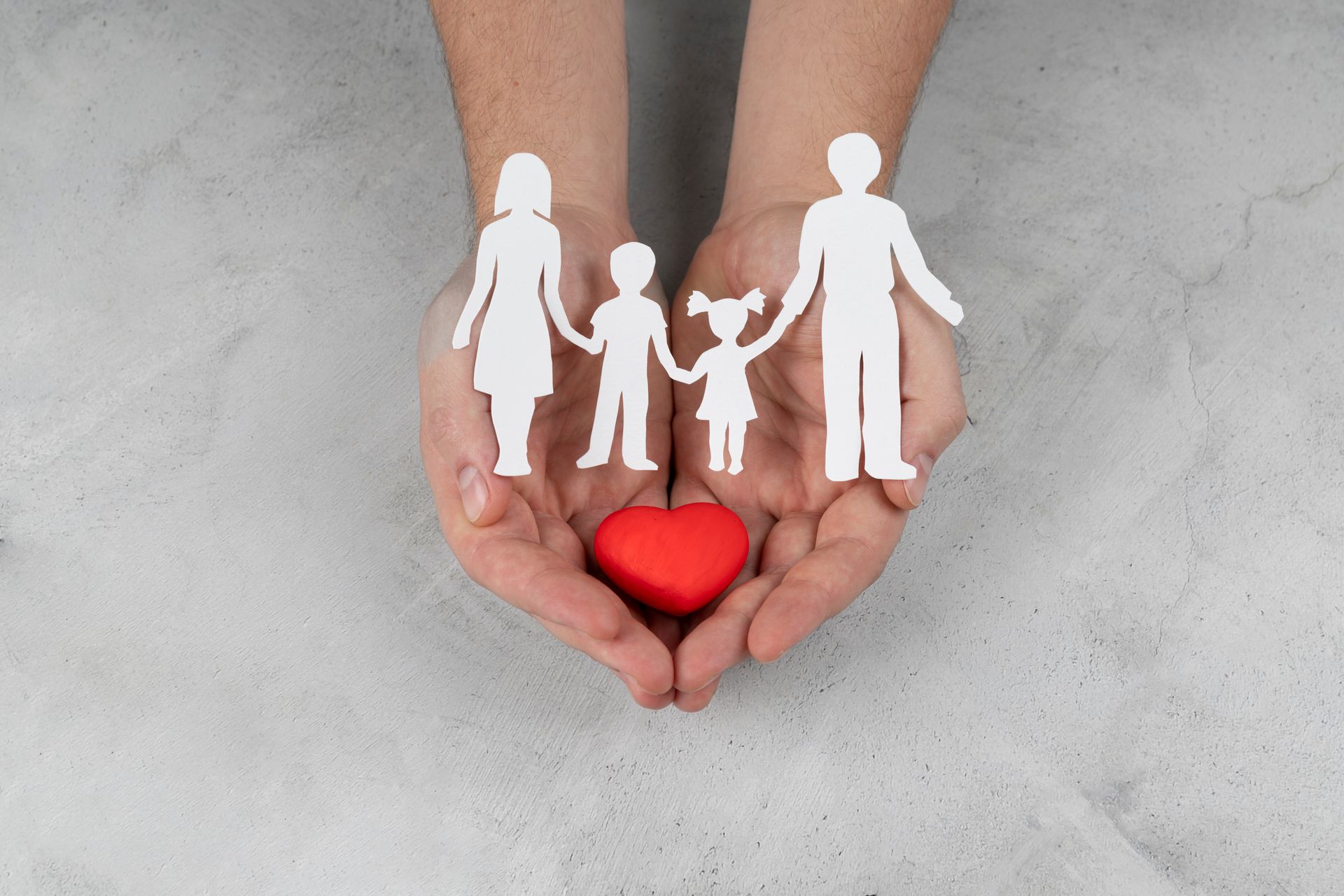 Mãos segurando um coração vermelho e uma família de papel recortado, simbolizando amor e carinho.