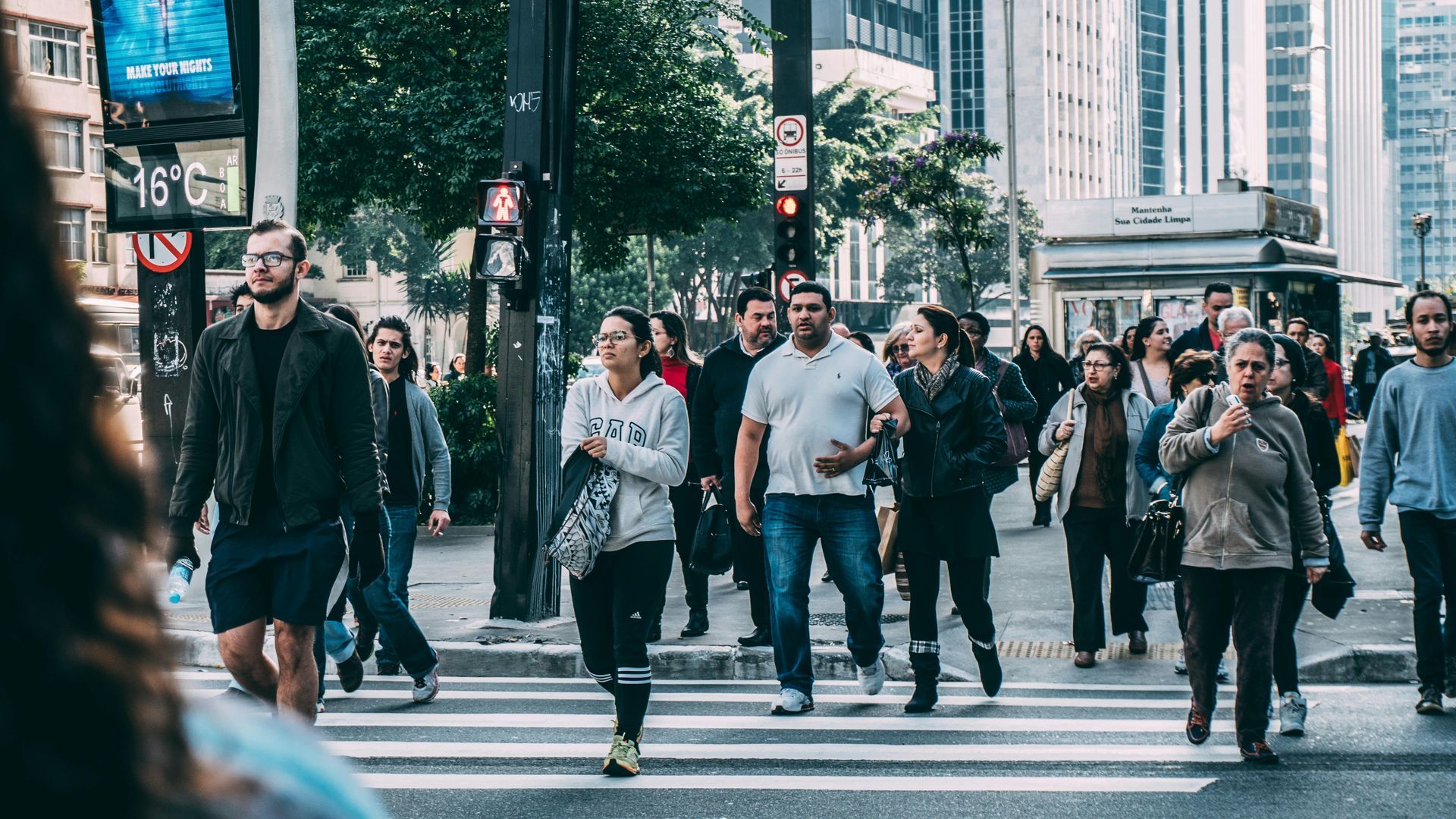 People crossing a city street at a crosswalk. Buildings in the background. Cloudy day.