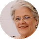 Mulher sorridente com cabelos grisalhos e óculos; colar de pérolas.