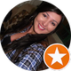 Mulher de cabelos longos e escuros, sorrindo, vestindo uma camisa xadrez; ícone de estrela laranja.