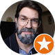 Homem de óculos e barba, vestindo um blazer, com um ícone de estrela laranja no canto.