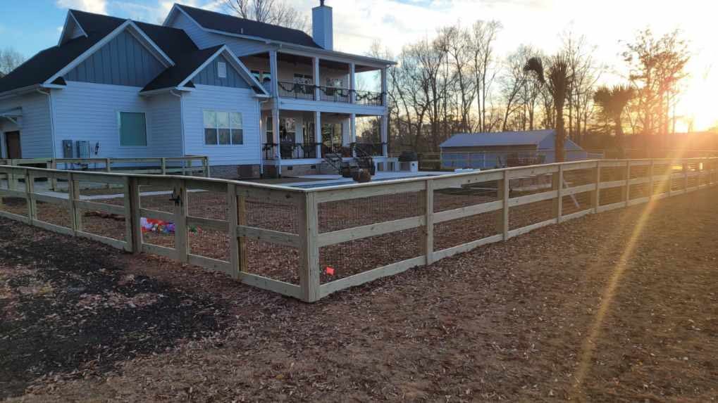 White farmhouse with porch and fenced yard at sunset, with bare trees and warm light.