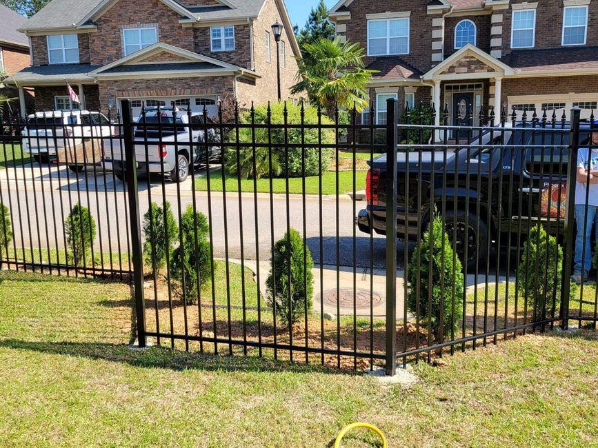 Black metal fence in front of suburban brick houses and parked vehicles on a sunny street