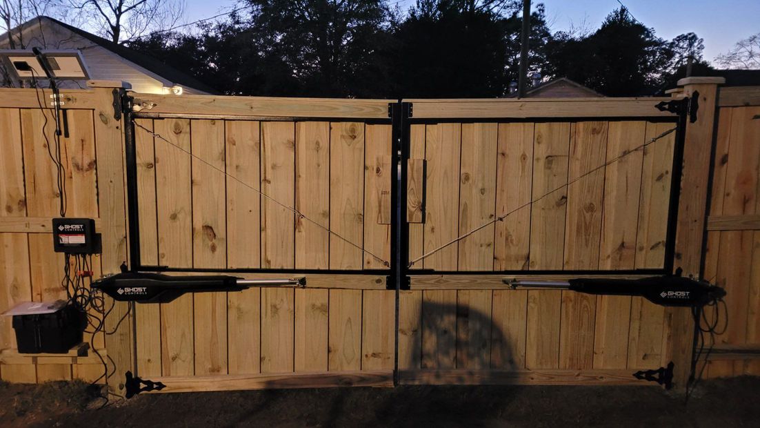 Wooden double gate with black metal hardware and mailbox at dusk, backed by houses and trees