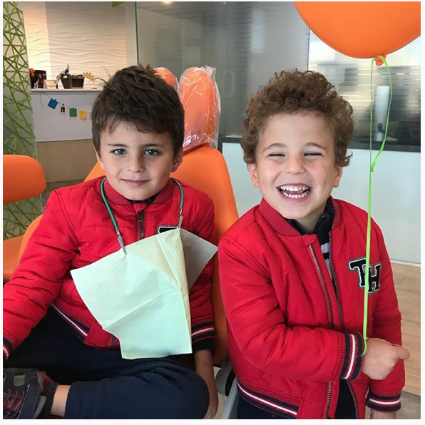 Two smiling boys in red jackets, one with a dental bib, the other holding an orange balloon.