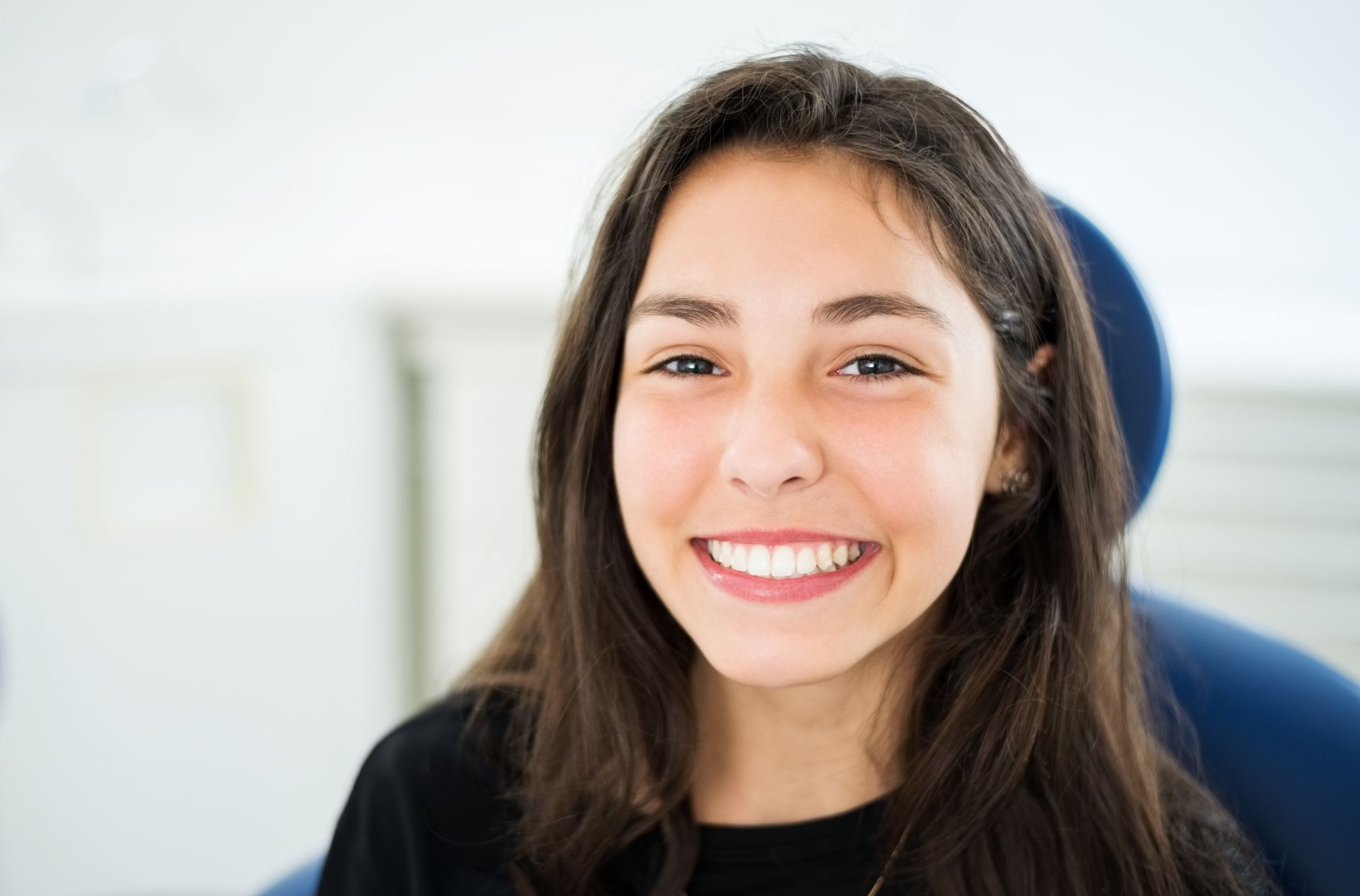 A young woman is smiling while sitting in a dental chair.