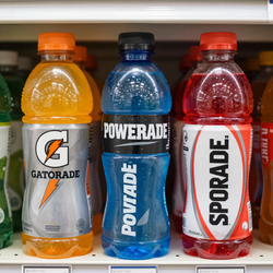 Tres botellas de bebida isotónica en un estante de una tienda: Gatorade naranja, Powerade azul y Sporade rojo.