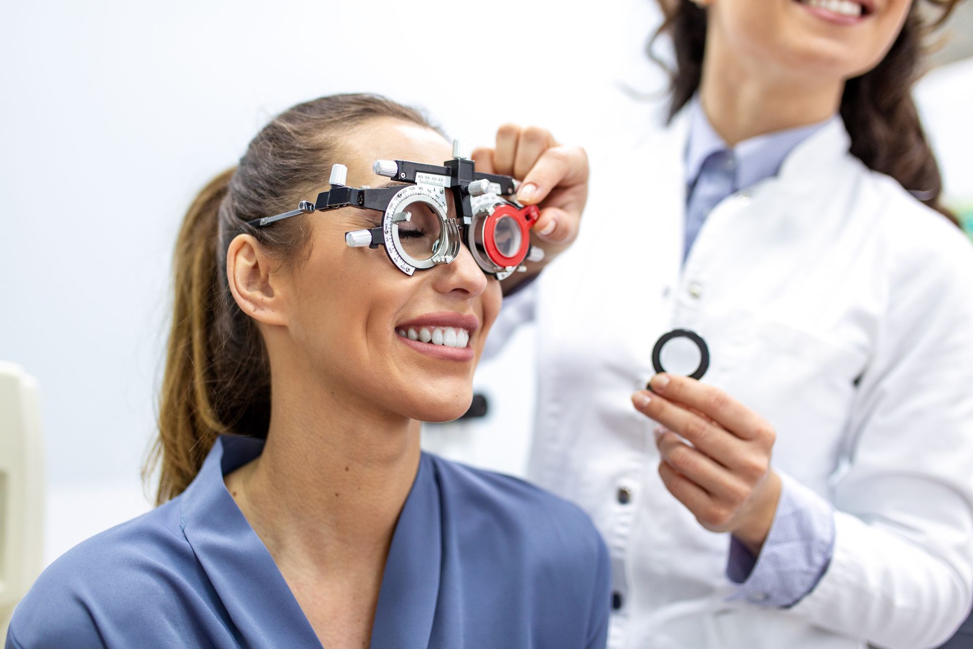 An optometrist adjusts a trial frame on a patient's face during an eye exam. An optometrist adjusts a trial frame on a patient's face during an eye exam.