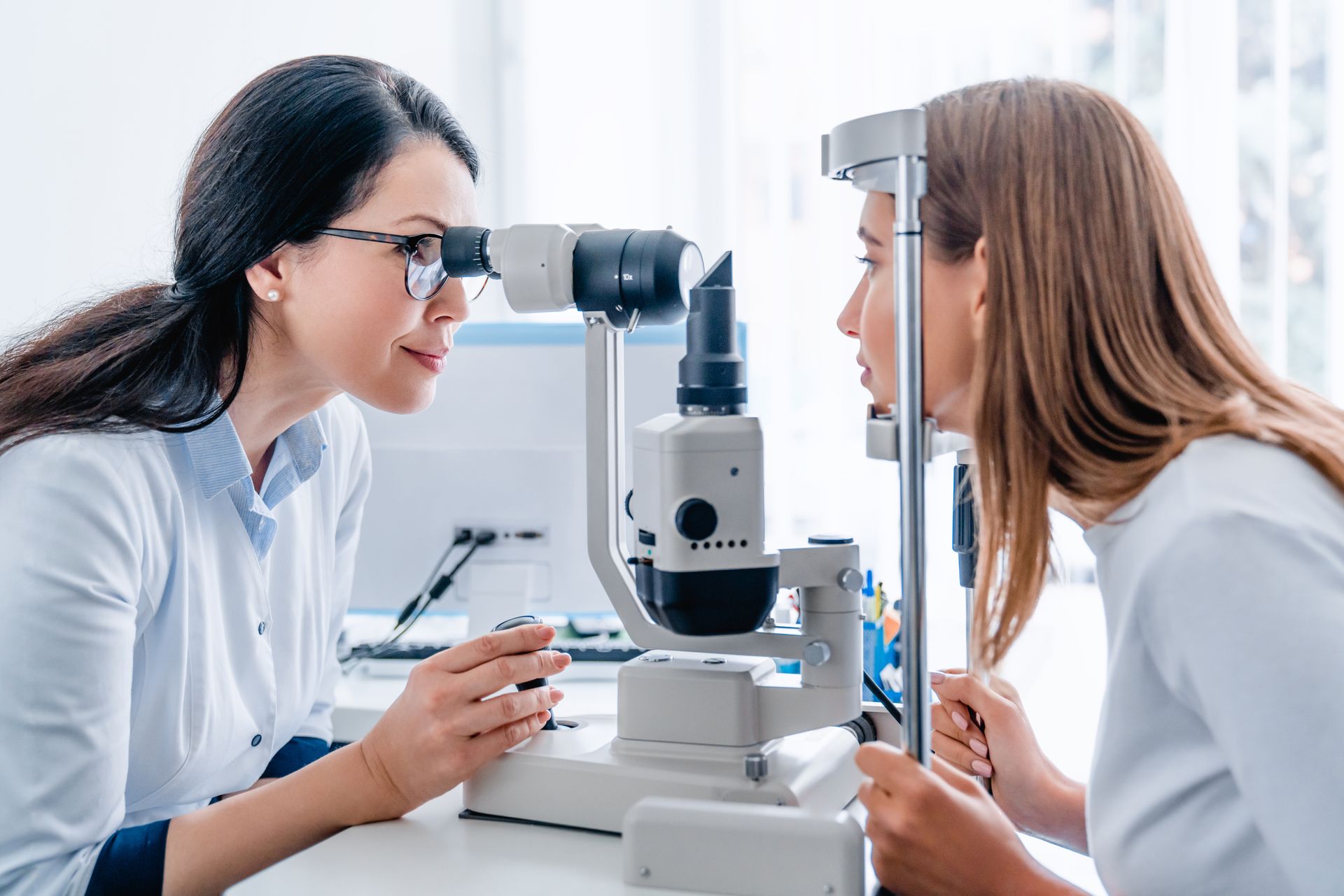 An optometrist performs an eye examination on a patient using a slit lamp microscope in a clinical setting. An optometrist performs an eye examination on a patient using a slit lamp microscope in a clinical setting.