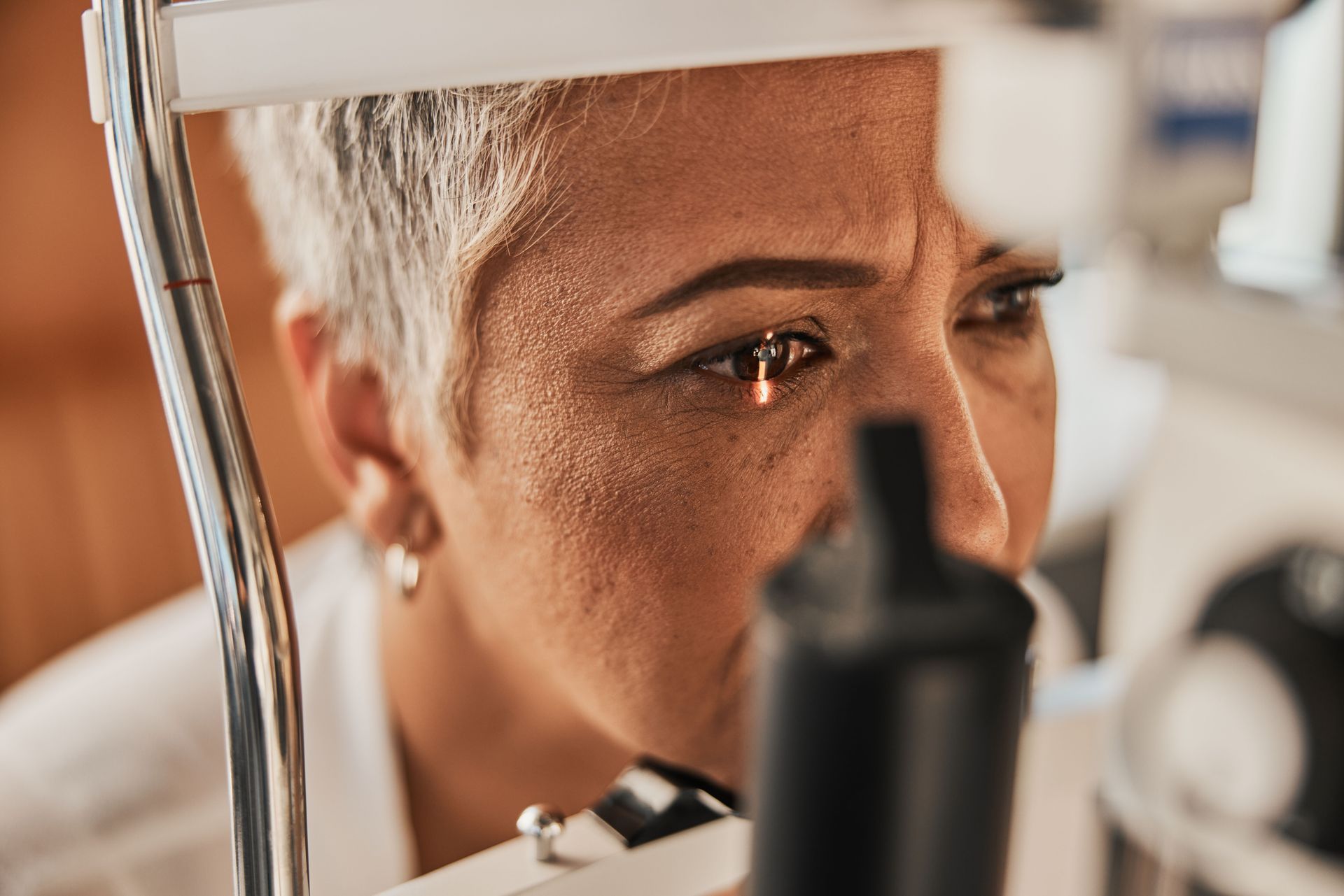 A person leans into a slit lamp microscope for an eye examination in a clinical setting. A person leans into a slit lamp microscope for an eye examination in a clinical setting.