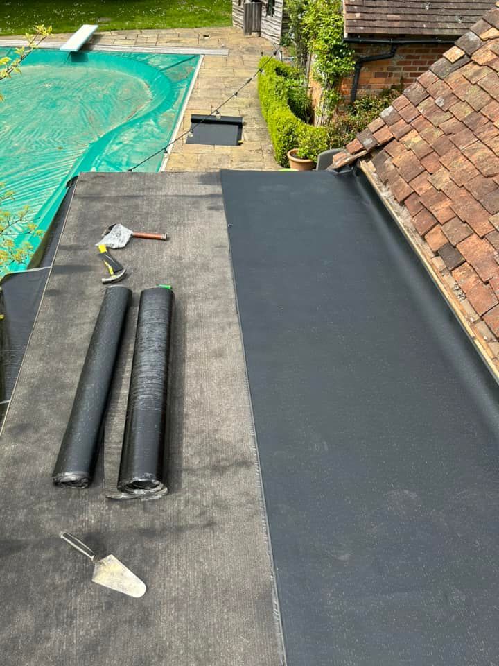 A roof with flat felt roof materials on it and tools beside them.