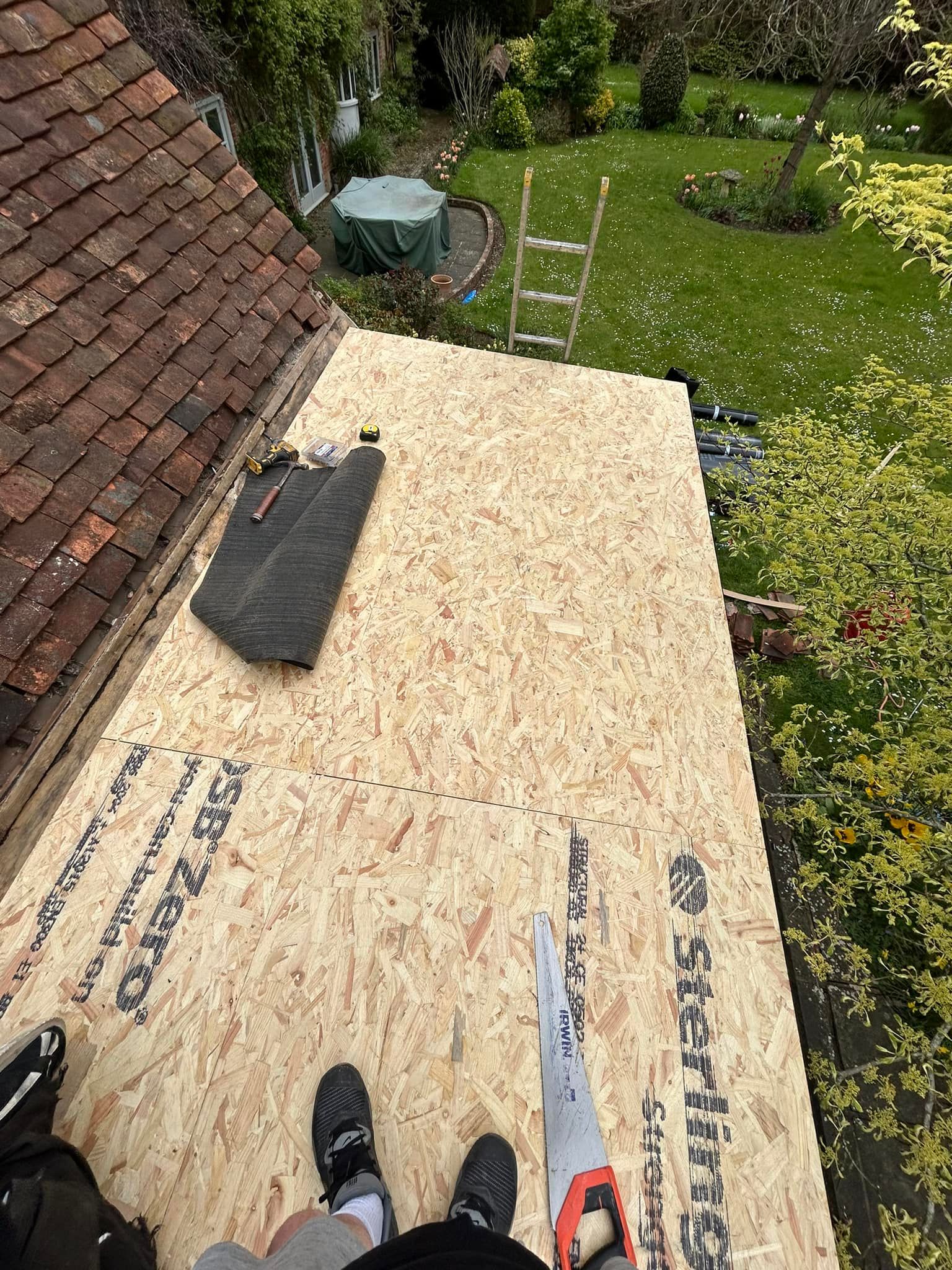 A person is standing on top of a wooden roof with a saw.