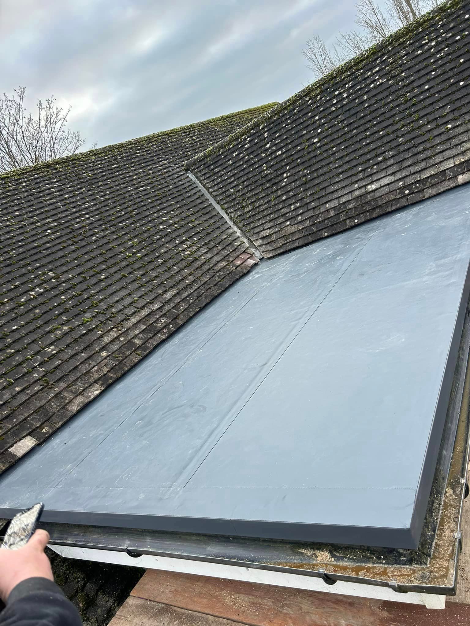 A modern flat roof is being installed next to a tiled roof