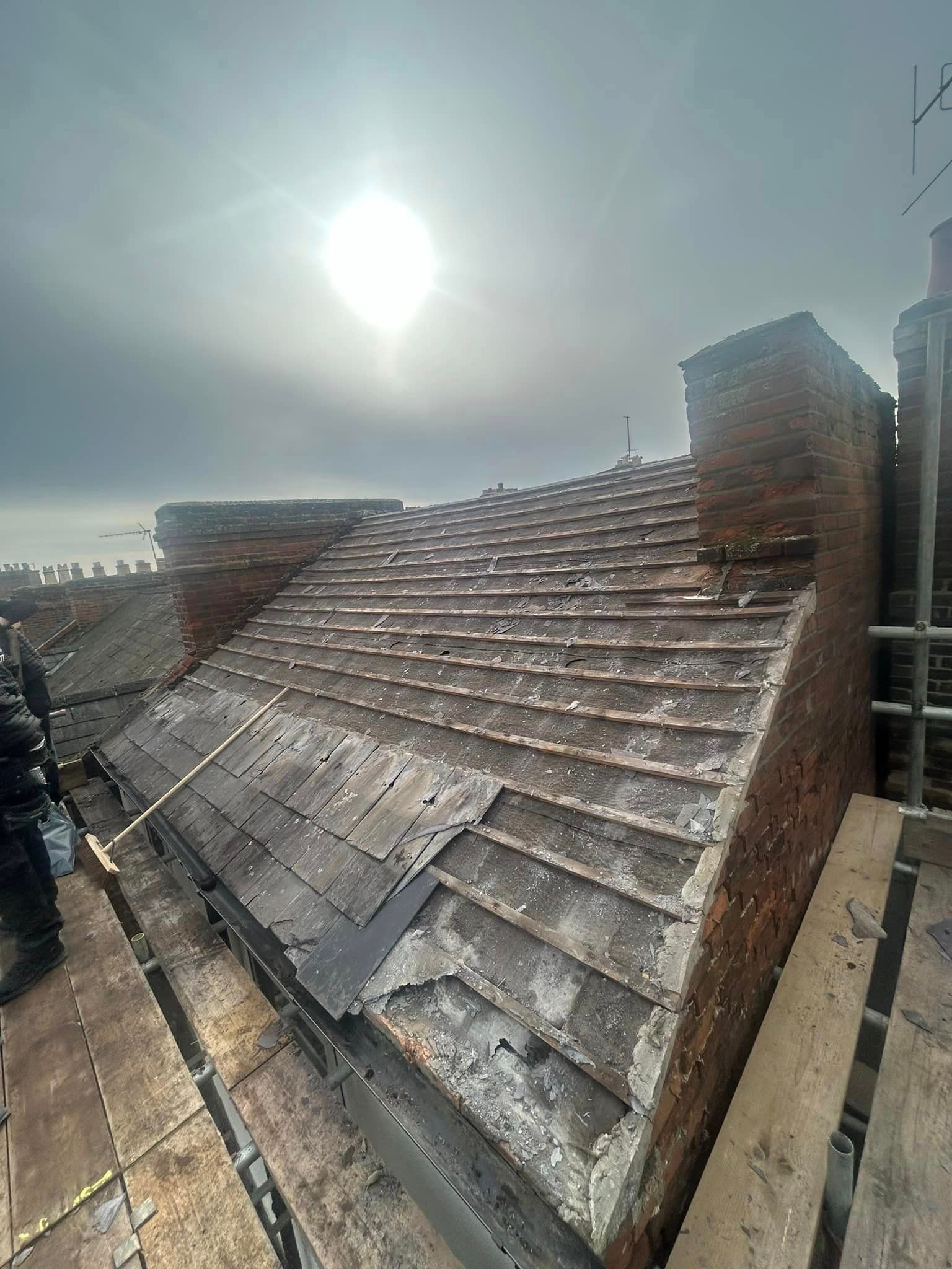 The roof of a building is being repaired and the sun is shining through the clouds.