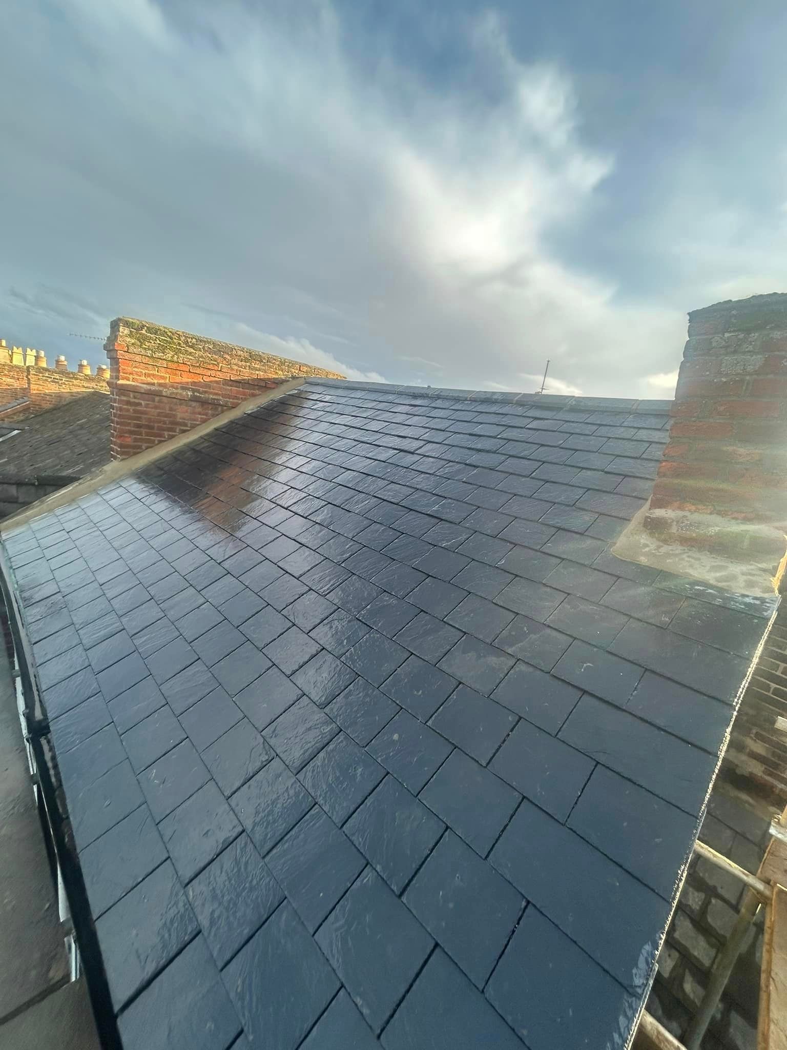 A slate roof on a house and a chimney in the background.