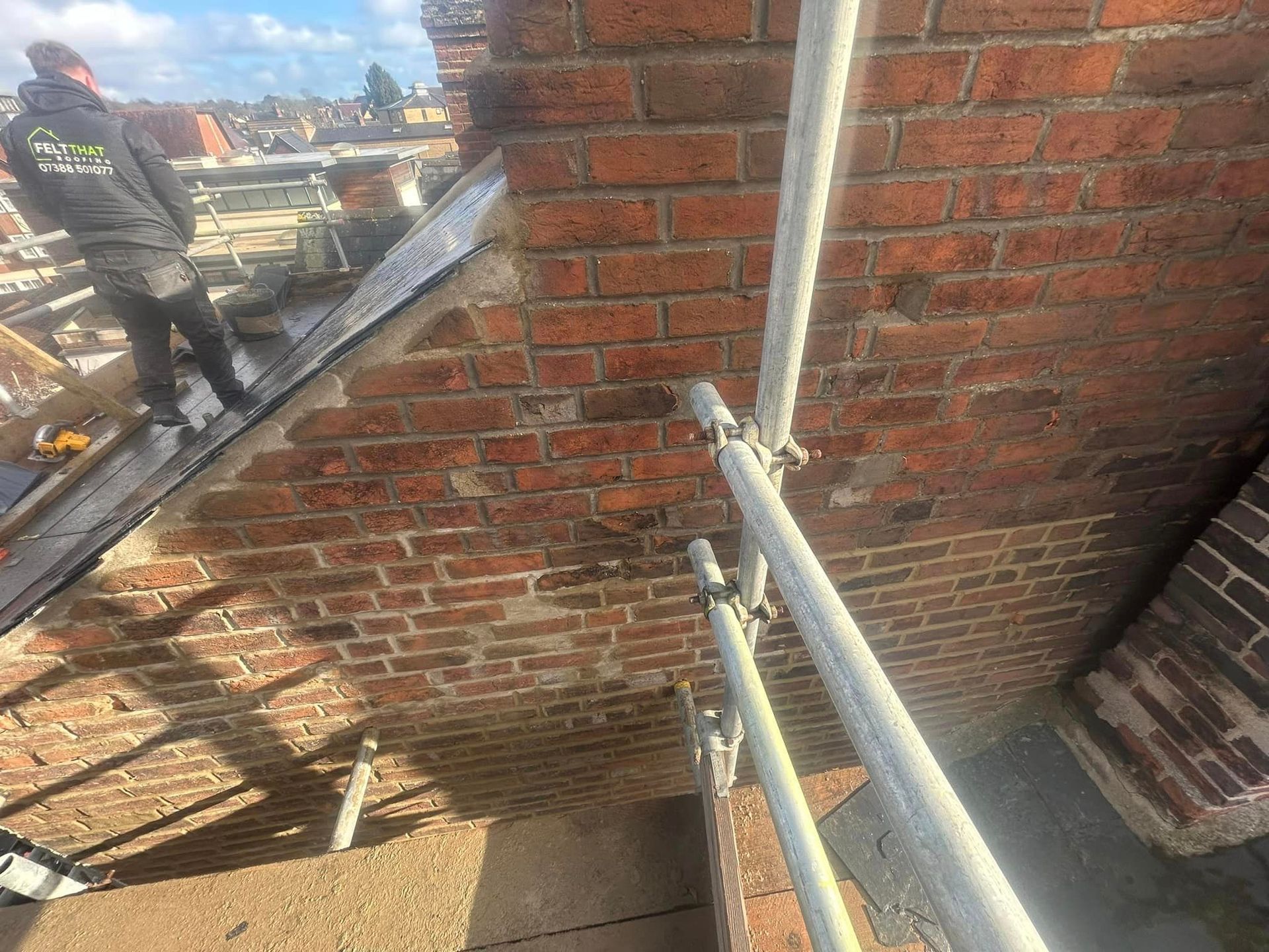A man is standing on a roof being repaired next to scaffolding