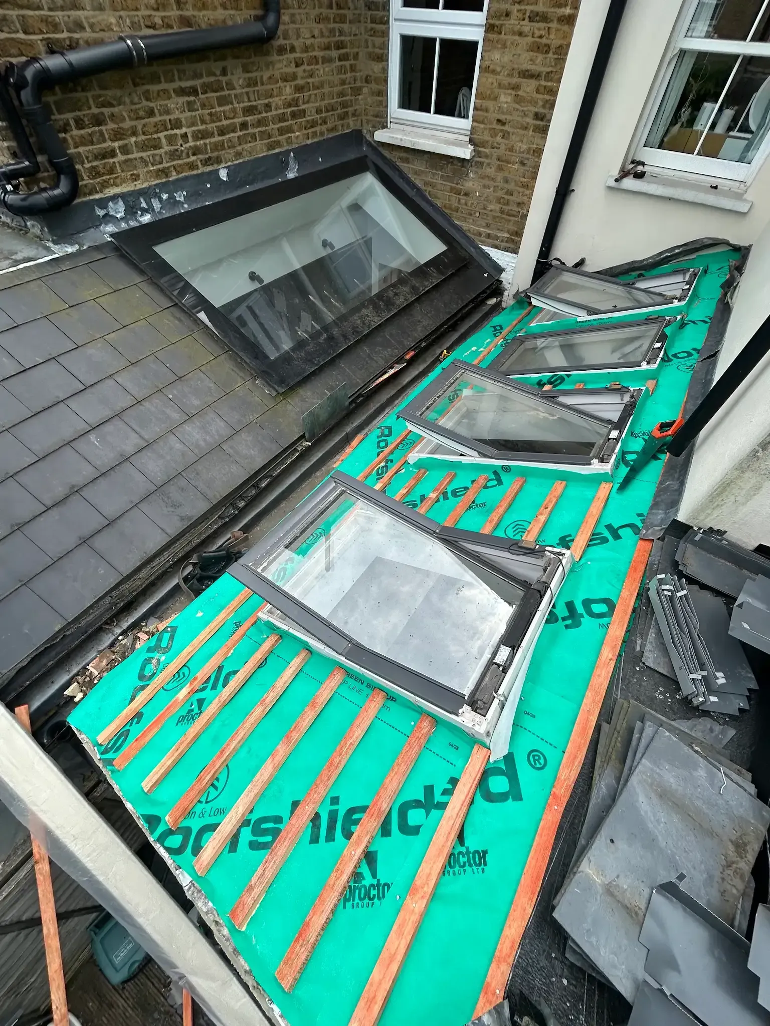 A roof with a green tarp on it and velux windows being installed