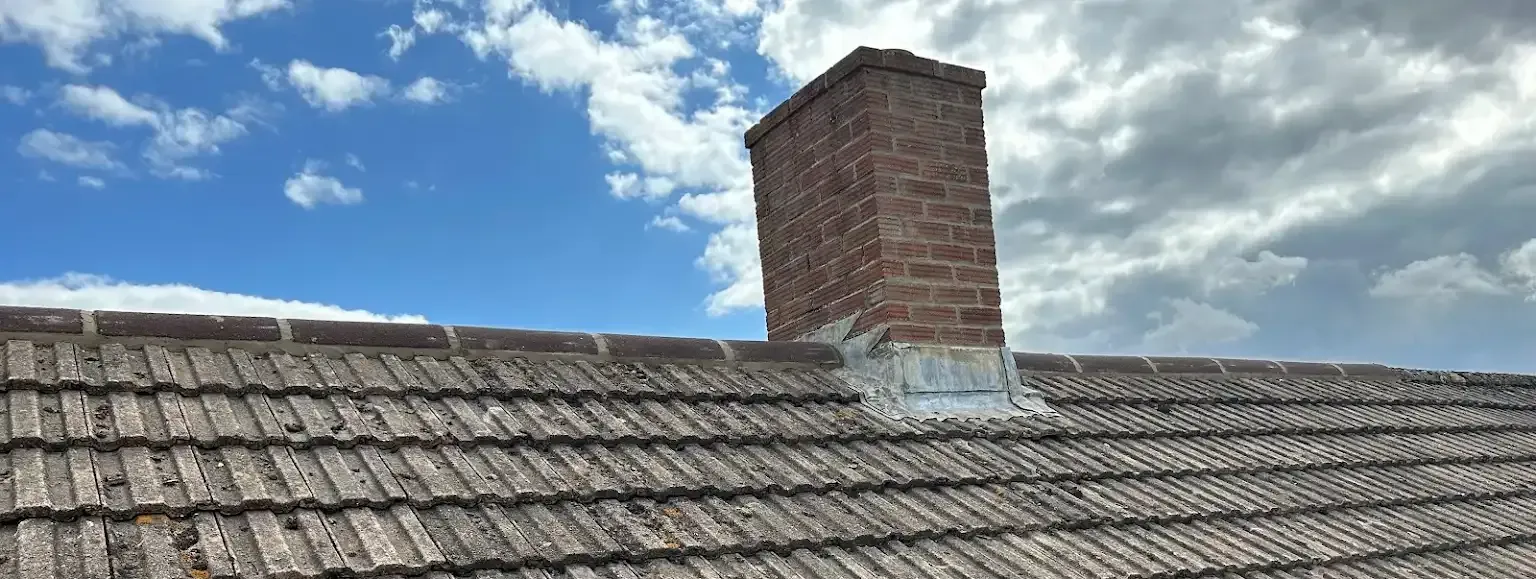 A brick chimney is sitting on top of a tiled roof.