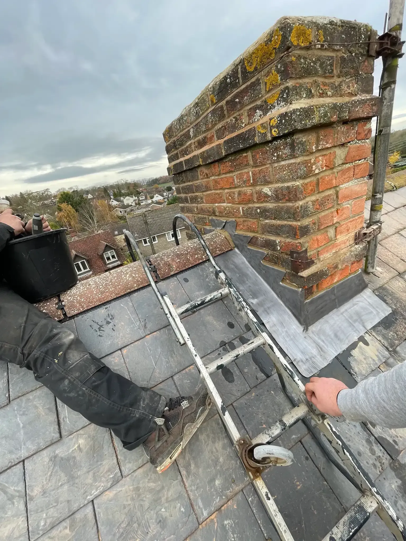 A roofer is repairing a roof next to a chimney.