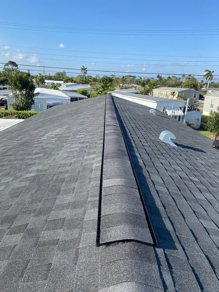 A view of a grey shingled roof ridge with a black ridge vent installed, set against a clear blue sky.