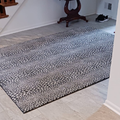 An indoor entryway with a patterned rug placed on light-colored tile flooring near a staircase and a small side table.