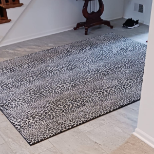 An indoor entryway with a patterned rug placed on light-colored tile flooring near a staircase and a small side table.